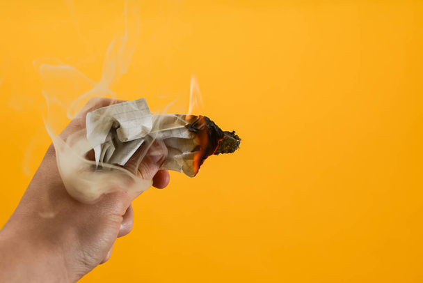 A small burning piece of paper with smoke from under the piece of paper. - Photo, Image