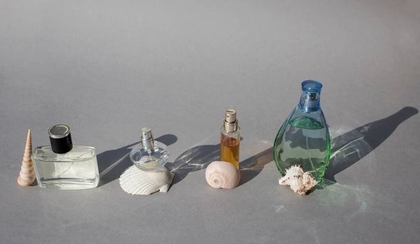 Diverses bouteilles de parfum féminines et masculines avec des coquilles intéressantes sur un fond gris avec des ombres dures debout dans une rangée. collection de parfumerie. Formes et ombres - Photo, image