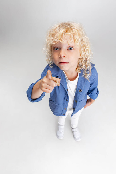Cute little curly preschool boy in casual clothes looking at camera isolated over white studio background. - Foto, immagini