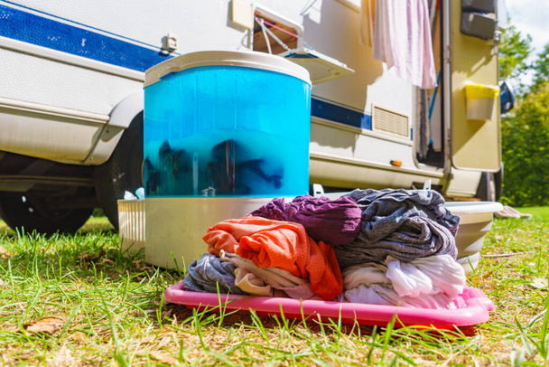 Doing laundry outdoor at caravan. Bowl with clean clothes and washing machine working. Camping on campground - Photo, Image