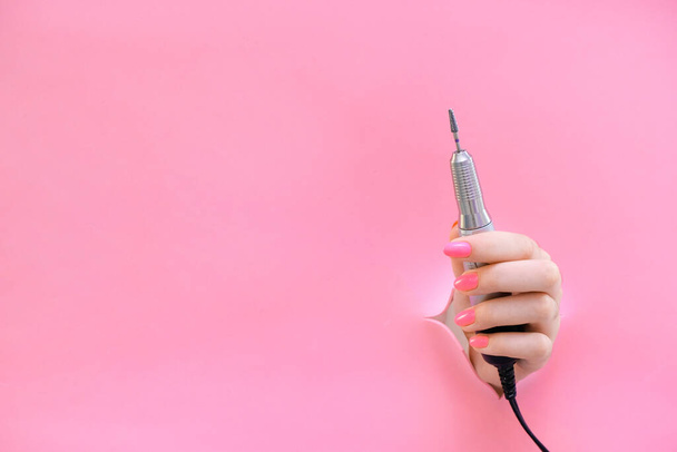 apparatus for manicure in the hand of a young woman on a pink background from a hole. hardwear manicure. copy space - Foto, Imagen