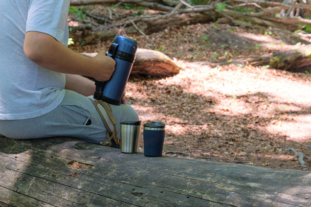Toeristisch eten voor buitenactiviteiten. Twee metalen thermo kopjes op een bosachtergrond. Geniet van een drankje tijdens reizen. - Foto, afbeelding