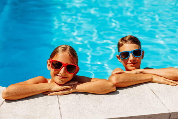 Happy kids in the pool, Funny kids in sunglasses playing outdoors, little boy and girl swim in the pool on a summer sunny day, Summer holiday concept - Foto, Imagen