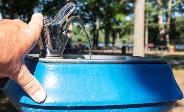 Закріпіть руку, натиснувши кнопку, щоб вода вийшла з старого блакитного джерела води в парку Белмонт Лейк Стейт Парку.. - Фото, зображення