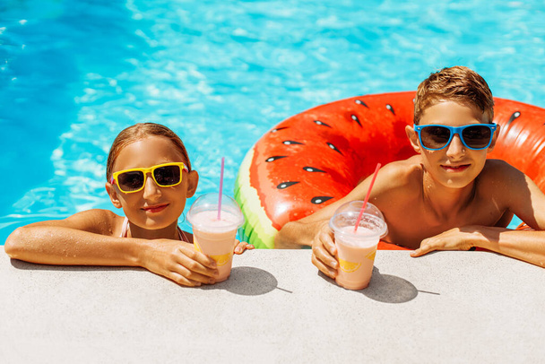 Close-up of cheerful little boy and girl in sunglasses drinking cocktails while enjoying in the pool, Cute brother and sister leaning on the edge of the pool and smiling, Summer holiday concept - Fotoğraf, Görsel