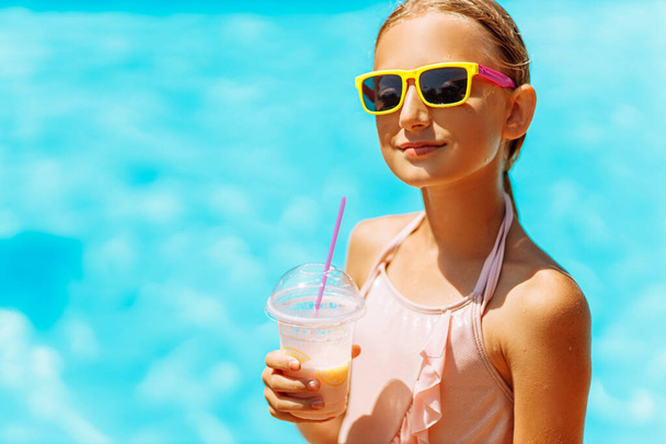 Маленька щаслива дівчинка в сонцезахисних окулярах п'є коктейль на відпочинку біля басейну під час відпустки в теплій тропічній країні, в сонячний теплий літній день, концепція подорожей
 - Фото, зображення