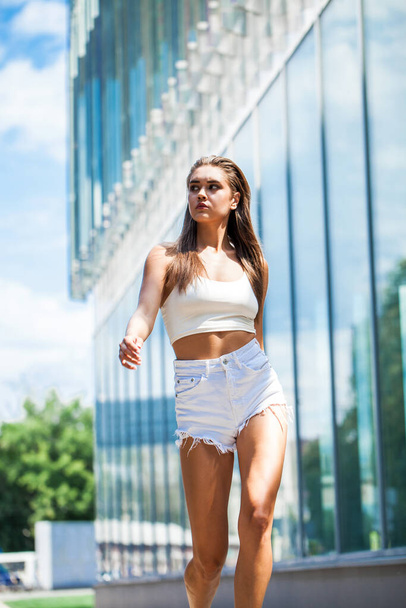 Full body portrait of a young beautiful brunette girl walking in summer street - Zdjęcie, obraz