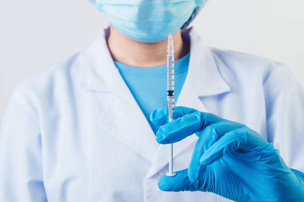 Injectienaald van covid-19 vaccin in professionele wetenschapper of arts hand in lab voor behandeling met masker handschoenen labjas op witte achtergrond. Begrip "gezondheidssector". - Foto, afbeelding