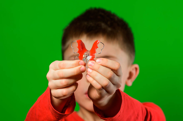 A boy on a green background shows his plate for aligning teeth. new - Photo, Image