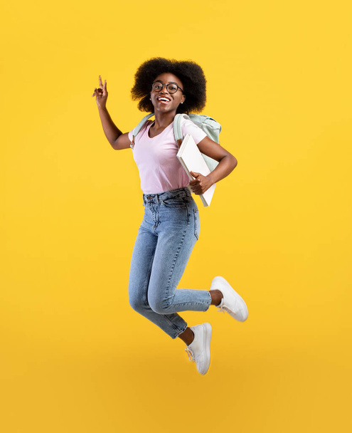 Enjoying student life. Full length portrait of african american lady jumping, wearing backpack and holding notepads - Foto, Imagem