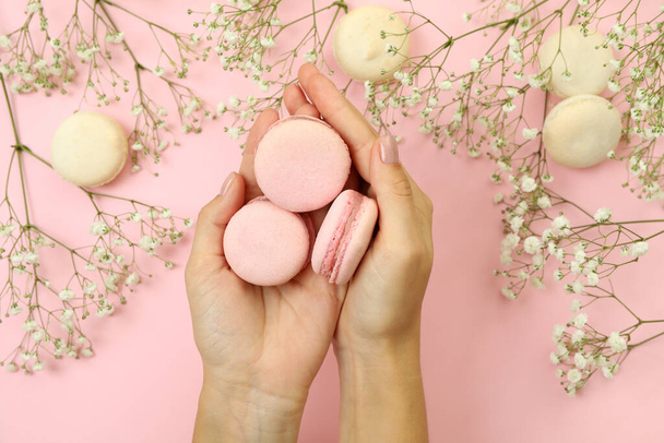 Female hands hold macaroons on pink background with macaroons and flowers - Foto, afbeelding
