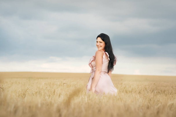 A girl in a dress with long hair in a wheat field in the evening dramatic light. - Φωτογραφία, εικόνα
