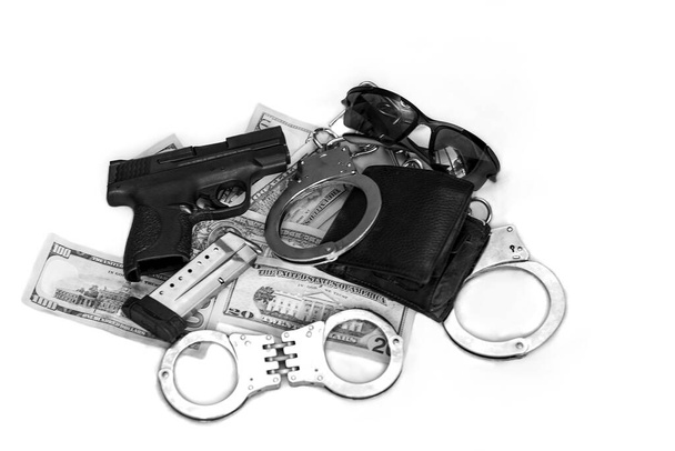 Gun and money. 9 mm pistol gun bullets strewn and dollar banknotes on white. Semi Automatic handgun firearm with mags and rounds, leather wallet in a pile of dollar bills with handcuffs and sunglasses Gun and money. 9 mm pistol gun bullets strewn  - Photo, Image