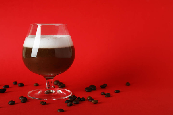 Egy pohár ír kávé és kávészemek piros alapon - Fotó, kép