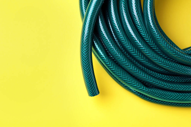 Green rubber watering hose on yellow background, top view. Space for text - Foto, Imagem
