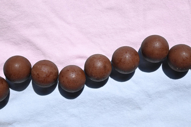Chocolates esféricos dispuestos en una fila, fondo de color pastel - Foto, imagen