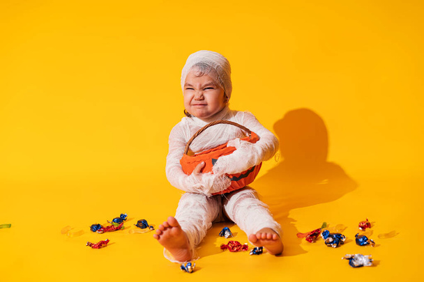 Criança em traje de múmia segura cesta na forma de abóbora com doces em suas mãos. - Foto, Imagem