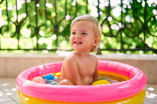 Маленький улыбающийся малыш сидит в маленьком надувном бассейне - Фото, изображение