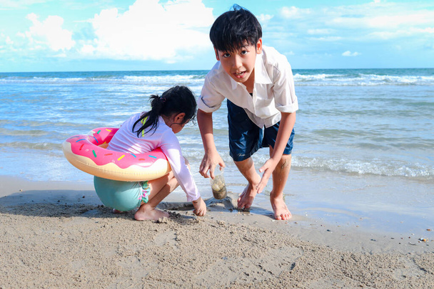 Dva roztomilé děti chlapec a dívka baví společně na písečné letní pláži s modrým mořem, šťastný dětství přítel hraje s pískem na tropické pláži, bratr a sestra tráví čas na rodinné dovolené. - Fotografie, Obrázek