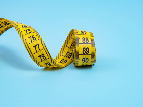 Yellow spiral tape measure on blue bright background - Photo, Image