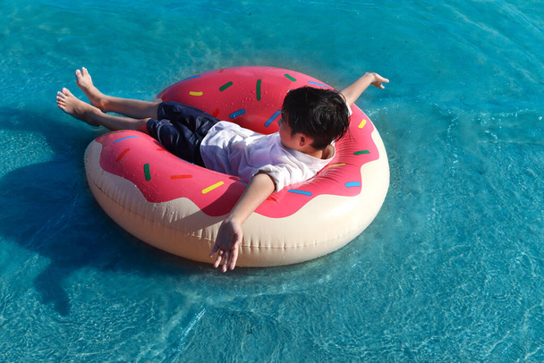 Egy boldog fiú színes felfújható úszógyűrű lebeg a felszínen, és hullám a trópusi kék tenger, gyerek időt tölt, és jól érzi magát a nyári vakáció, jól érzi magát, és pihenni hétvégén.  - Fotó, kép