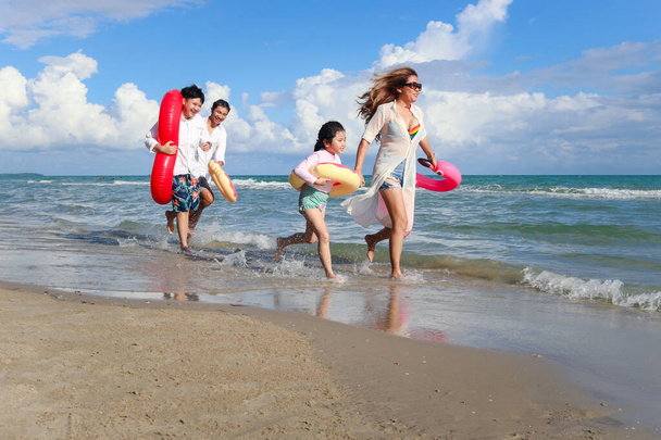 Kinder mit Eltern tragen bunte aufblasbare Schwimmringe, die am Sommerstrand laufen, Kinder und Erwachsene am tropischen Sandstrand, glückliche Familien verbringen Zeit und Spaß zusammen im Sommerurlaub.  - Foto, Bild