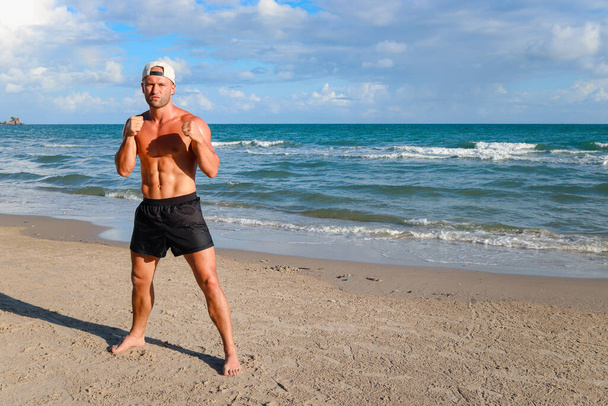 Πορτρέτο της ισχυρής αθλητική προπόνηση μποξέρ και punching στην παραλία, νεαρός όμορφος μυώδης fitness man κάνει ασκήσεις πυγμαχίας εξωτερική άσκηση για το καλοκαίρι τροπικό νησί παραλία - Φωτογραφία, εικόνα