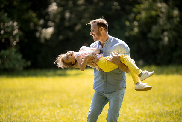 Отец с милой маленькой дочкой веселится на траве в парке - Фото, изображение
