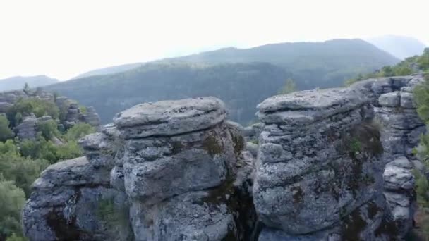 Szürke sziklás képződmények az ég és a hegyek hátterében. - Felvétel, videó