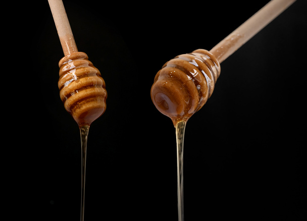 Μέλι με ξύλινο ραβδάκι που απομονώνεται σε μαύρο φόντο. Γλυκό φαγητό. Μέλισσες και κερί. Νέκταρ. - Φωτογραφία, εικόνα