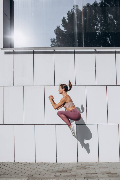 Vue de côté image de la jeune femme caucasienne sportive mince travailler, faire du fitness, yoga dans la rue de la ville. - Photo, image