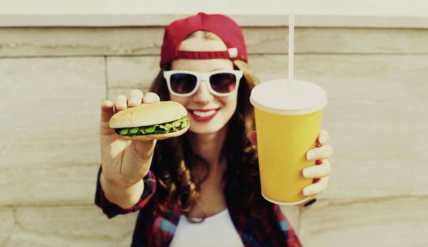 Portrait of happy smiling young woman with burger and cup of juice fast food in the city - Zdjęcie, obraz