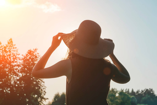 Szczęśliwa dziewczyna w kapeluszu cieszy się życiem na słonecznym polu lata. Styl życia, lato, relaks, koncepcja podróży - Zdjęcie, obraz
