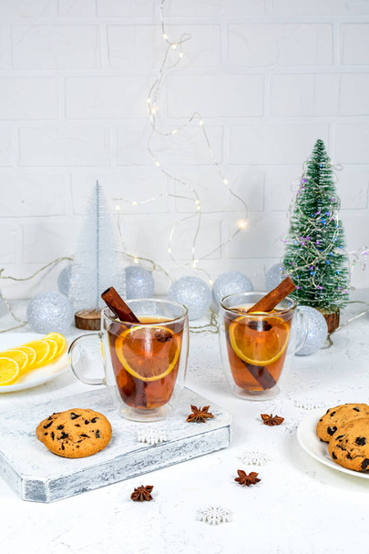 Χριστουγεννιάτικη κάρτα Πρωτοχρονιάς. Δύο ποτήρια τσάι με λεμόνι, κανέλα και γλυκάνισο στο φόντο του New Years New Years με γιρλάντες, μπάλες και τεχνητά χριστουγεννιάτικα δέντρα. - Φωτογραφία, εικόνα