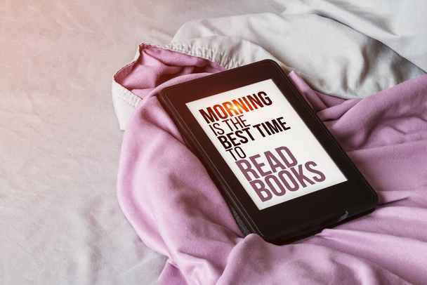 Moderni e-lukija sähköinen kirja, jossa teksti ruudulla - aamu on paras aika lukea kirjoja - on harmaa ja violetti sänky auringonvalon linssi soihtu. Tabletti lainaus lukemisesta mikrokuituliina vuodevaatteet - Valokuva, kuva
