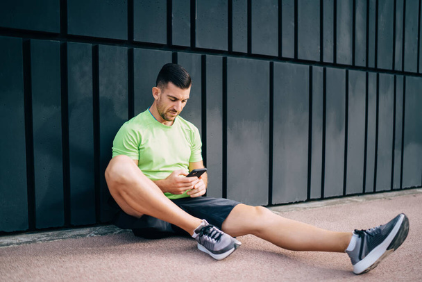 Caucasian male bodybuilder reading web publication about healthy lifestyle and mental wellness, young athletic runner using smartphone gadget with 4g wireless connection for browsing sportive website - Foto, Imagen