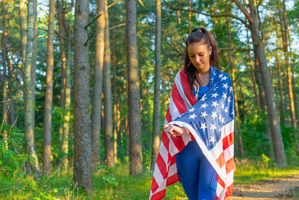 Bella ragazza con bandiera americana.Ragazza caucasica sexy con bandiera americana in mano sulla calda foresta estiva. - Foto, immagini