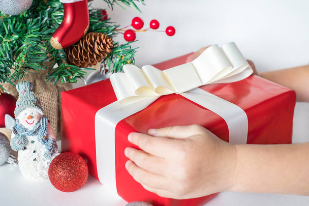 Дитячі руки на різдвяний подарунок біля маленької ялинки та прикраси на білому тлі
. - Фото, зображення