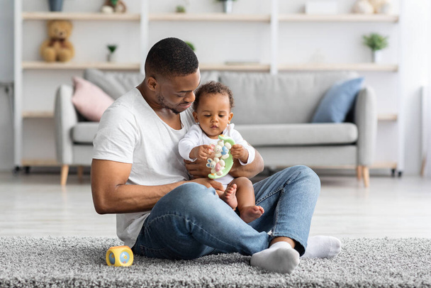 Αντίληψη πατρότητας. Ευτυχισμένος μαύρος άνδρας παίζει με αξιολάτρευτο βρέφος στο σπίτι - Φωτογραφία, εικόνα
