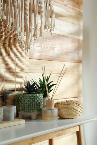 Air reed freshener, houseplant and decor on console table near wooden wall. Interior design - Fotoğraf, Görsel