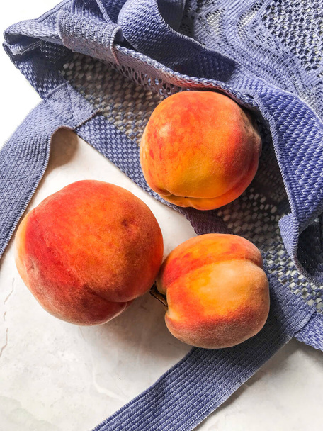 Beautiful juicy peaches in a textile bag on a light wooden table, natural ecological food and a reusable bag - Foto, afbeelding