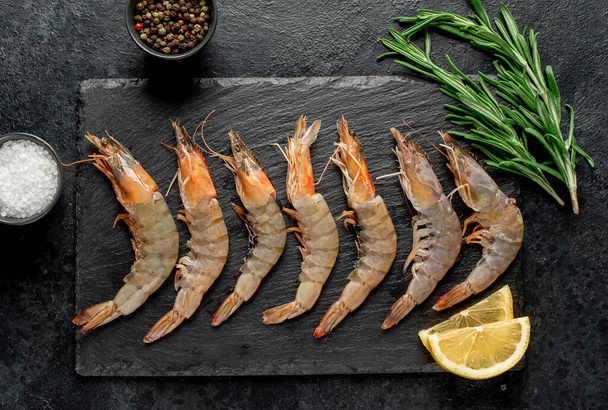 raw fresh shrimps with lemon and rosemary on black background. top view. - 写真・画像
