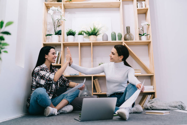 Full body of happy female coworkers congratulating each other and giving high five after successful online work with documents together - Foto, Bild