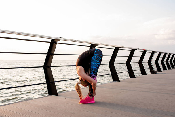 young woman doing yoga on the embankment at dawn with the view of the ocean. - Foto, immagini