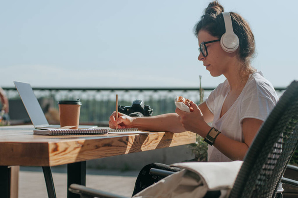 Freelancer feminina usando fones de ouvido escrevendo fazendo anotações trabalhando no laptop. Conceito de geração Z. - Foto, Imagem