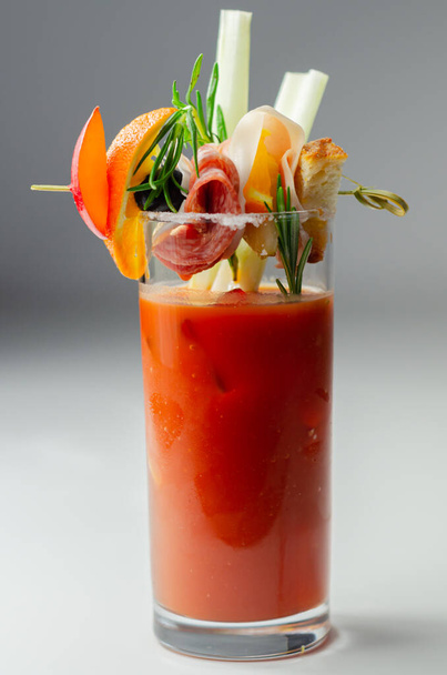 Bloody Mary érdekes dekorációval, egy kis harapnivalóval egy koktélpohár tetején, frissítő ital. - Fotó, kép