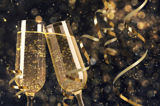 Glasses with sparkling wine and shiny serpentine streamers against blurred festive lights  - Foto, imagen