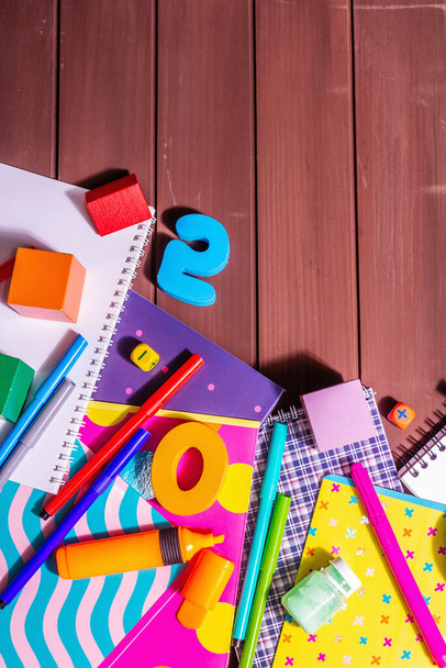 School supplies on wooden boards background. Album, notebooks, felt-tip pens, brushes, palette, wooden cubes and numbers. Fashion hard light, dark shadow, top view - Photo, Image