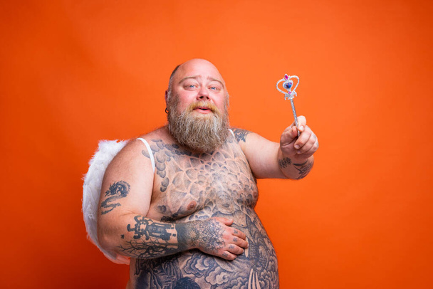 Gordo hombre feliz con barba, tatuajes y alas actúa como un hada mágica - Foto, Imagen