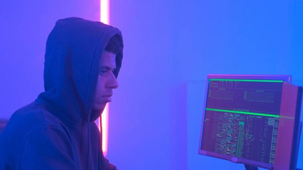 Profiel weergave van Afrikaanse hacker in hoodie werken in kamer gevuld met beeldschermen - Foto, afbeelding